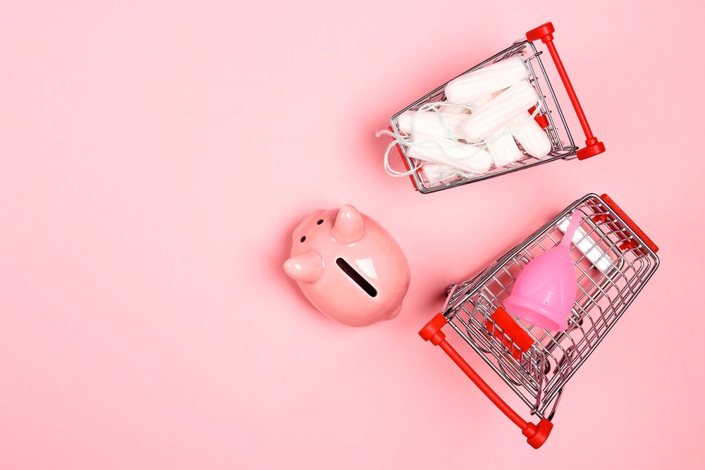 Sparschwein neben kleinen Einkaufswagen voller Tampons und Menstruationscup